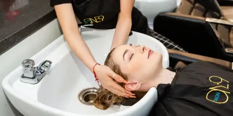 Woman receiving a hair wash at a salon sink, attended by a stylist.